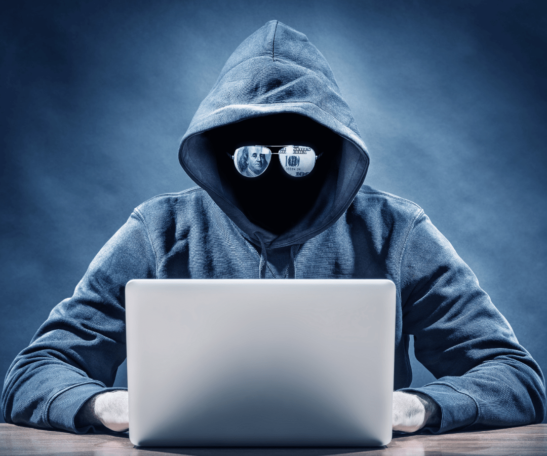 Hacker in hooded attire working on a laptop, symbolizing clandestine digital activities.